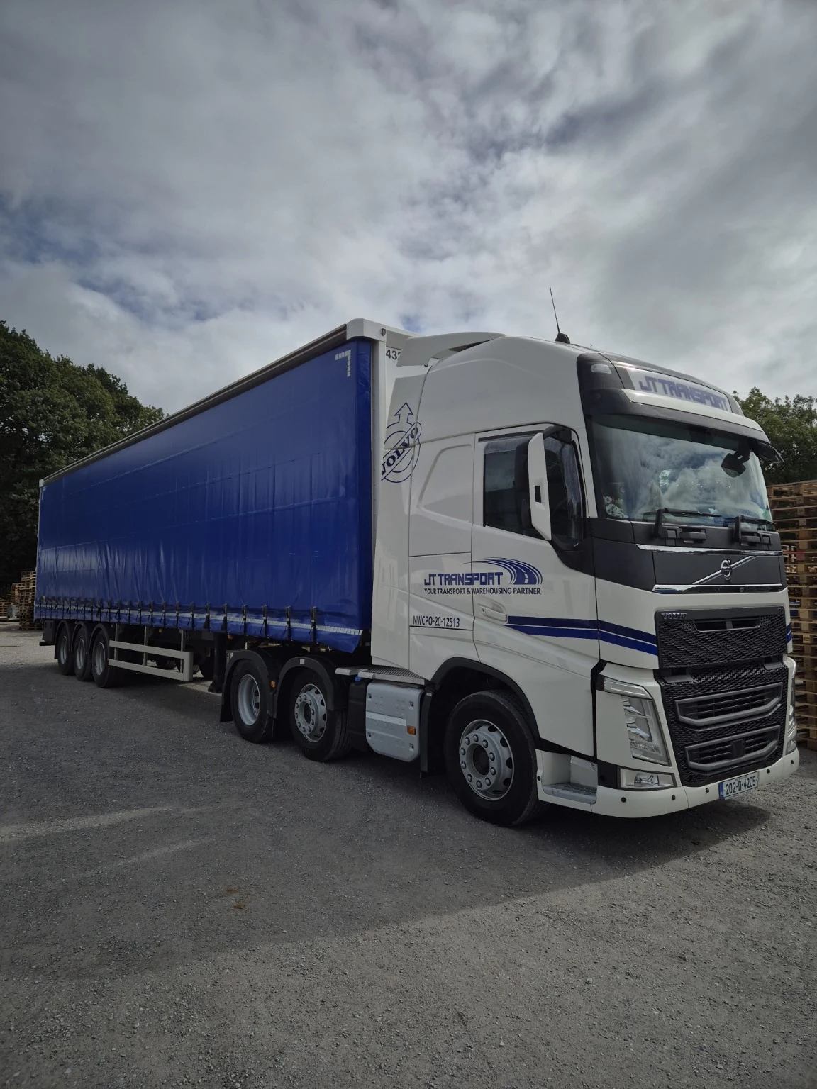 JT-branded Volvo tractor unit with a blue curtainsider trailer in the yard.