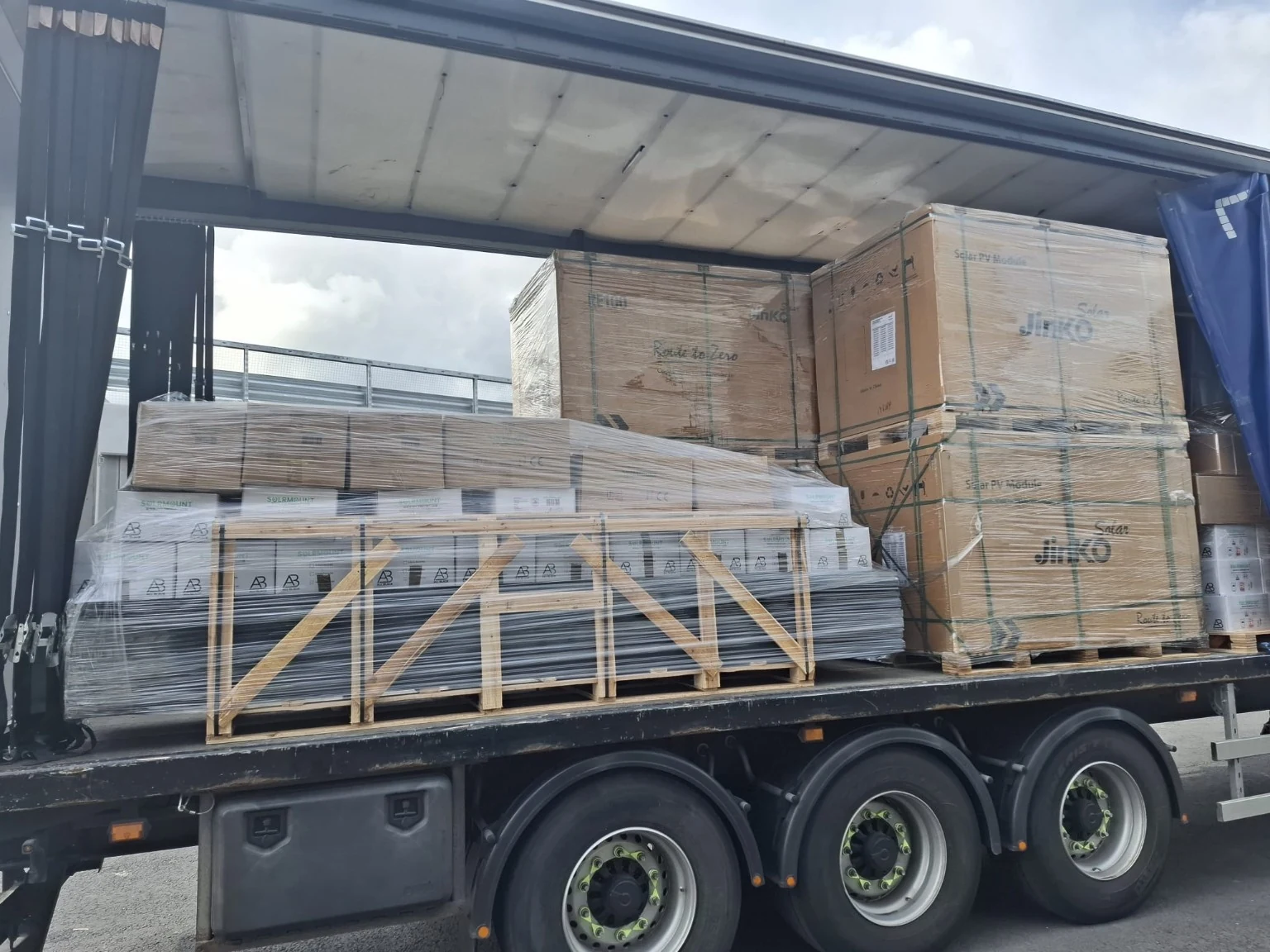Wrapped cartons and crated components on a curtainsider trailer.